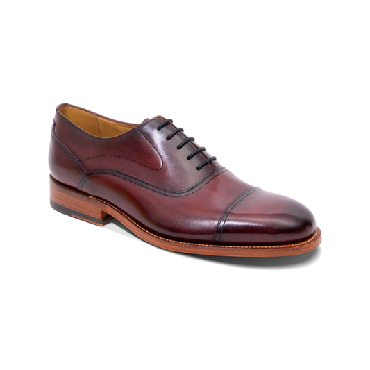 A single men's oxford dress shoe in glossy dark burgundy-brown leather, featuring a cap toe, black laces, and a stacked leather heel, shown on a plain white background.
