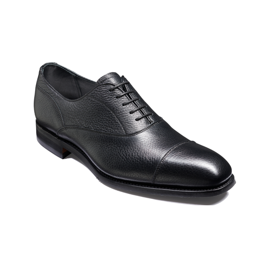 A black leather cap-toe oxford shoe with a pebbled texture, black laces, and a low stacked heel, shown from a three-quarters angle on a white background.