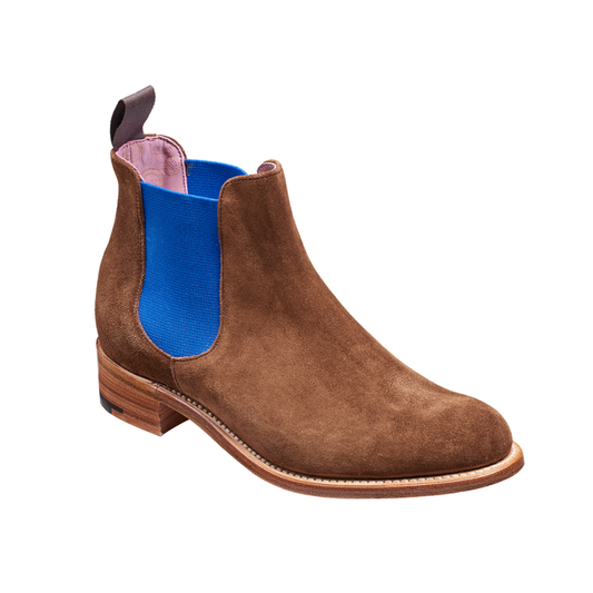 A brown suede Chelsea boot with a bright blue elastic side panel and a low stacked heel, shown from a three-quarters angle on a white background.